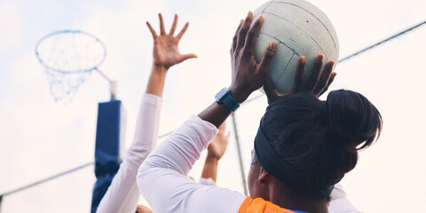 Netball, goal shooter and fitness of a girl athlete group on an outdoor sports court. Aim, sport game and match challenge of a black person with a ball doing exercise and training in a competition.