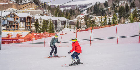 Boy learning to ski, training and listening to his ski instructor on the slope in winter.